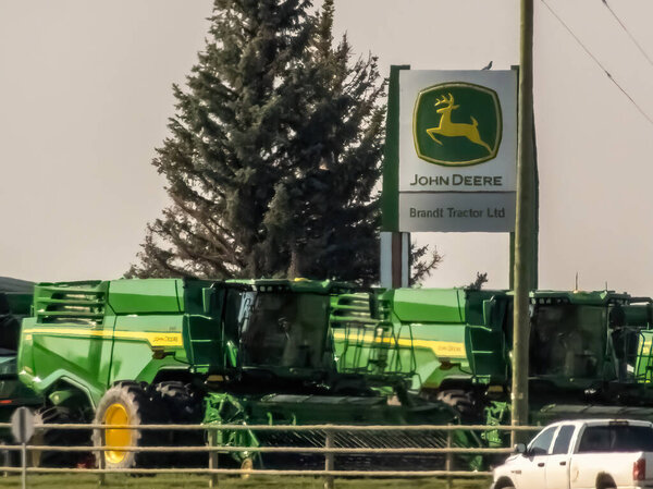 Alberta, Canada. Aug 24, 2024. A John Deere dealership sign stands prominently above a row of green agricultural machinery.