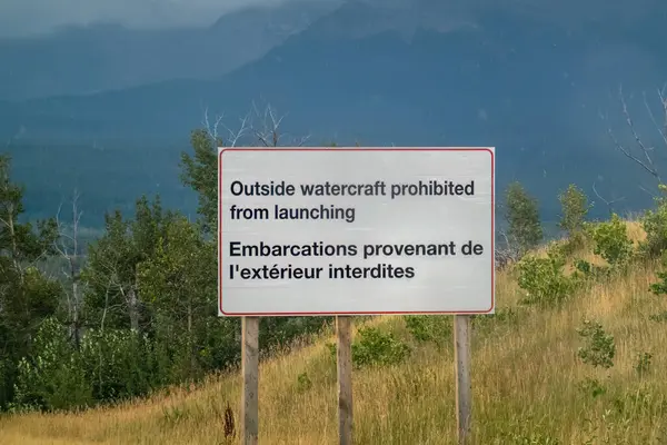 Waterton Park, AB, Kanada. Ağustos 24, 2024. Kırmızı harfli beyaz bir tabela, bölgeden suya indirmeye karşı uyarıda bulunuyor. İşaret İngilizce ve Fransızca metinlerle iki dillidir..