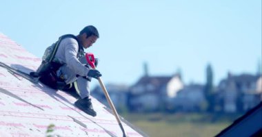 Calgary, AB, Kanada. 19 Eylül 2024. Bir inşaat işçisi eğimli bir çatıda çatıdaki küreği dikkatlice kullanıyor, açık gökyüzünün altında güvenlik donanımı giyiyor. Endüstriyel çatı küreği.