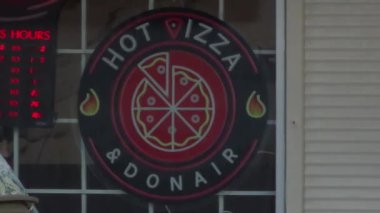 Calgary, AB, Kanada. 19 Eylül 2024. Canlı bir neon ışığı, Hot Pizza ve Donair 'ın reklamını yapan bir mağaza önünü aydınlatıyor. Dairesel tasarım, pizza dilimleri ve alevler içinde müşterileri davet ediyor..