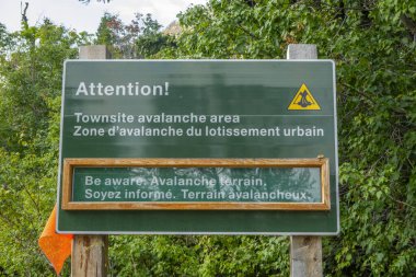 Waterton Park, AB, Kanada. 19 Ağustos 2024. Yeşil uyarı işareti, ziyaretçileri bir şehir merkezindeki çığ tehlikesine karşı uyarır. Tabelada hem İngilizce hem de Fransızca metin ve grafik uyarı yer alıyor..