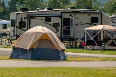 Waterton Park, Alberta, Kanada. 20 Ağustos 2024. Güneşli bir kamp alanındaki büyük bir karavanın yanında geleneksel ve modern kamp deneyimlerinin bir karışımını sunan bir çadır duruyor..