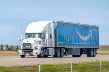 Calgary, Alberta, Kanada. 2 Ekim 2024. Beyaz bir kamyonet otobanda büyük mavi bir Amazon Prime karavanı taşıyor, ikonik Amazon gülümseme logosu ve aerodinamik tasarım içeriyor.