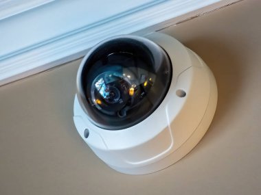 Tavana monte edilmiş beyaz bir kubbe güvenlik kamerası ve çevreyi yansıtan siyah bir lens..