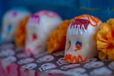 Karmaşık kremalarla bezenmiş ve canlı kadife çiçekleriyle çevrili renkli şeker kafatasları Ölüler Günü 'nü canlandırıyor..