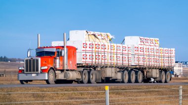 Calgary, Alberta, Kanada. 2 numara, 2024. Düz karavanı olan kırmızı bir yarı kamyon. Otoyol boyunca bir sürü inşaat malzemesi taşıyor..