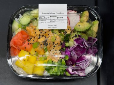 Calgary, AB, Canada. Oct 30, 2024. A clear container filled with an appetizing looking Sriracha Salmon Poke Bowl with white rice, salmon, avocado, red cabbage, yellow bell peppers and green onions. clipart