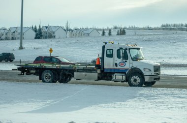 Calgary, Alberta, Kanada. 9 Aralık 2024. Karlı bir yolda üzerinde CAA logosu olan beyaz bir çekici, bir arabayı çekiyor..