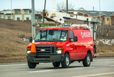 Calgary, Alberta, Kanada. 18 Ocak 2025. Versalift hava çalışma platformu ve Rogers tabelası olan kırmızı bir Ford E-Serisi servis minibüsü yol boyunca gidiyor..