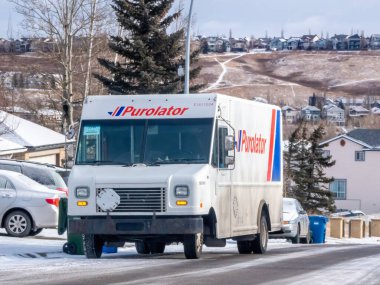 Calgary, Alberta, Kanada. 18 Ocak 2025. Beyaz bir Purolator dağıtım aracına yakın bir araç yerleşim alanına yakın bir yol boyunca ilerliyor. Kamyonun yan tarafında belirgin bir Purolator logosu var..