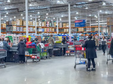 Calgary, Alberta, Kanada. 18 Ocak 2025. Costco kasalarında müşteriler kuyrukta bekliyor, arabaları büyük miktarda malla dolu, yüksek raflarla çevrili..
