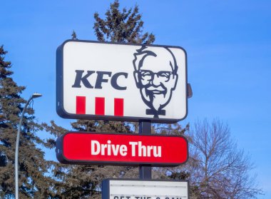 Calgary, Alberta, Kanada. 27 Ocak 2025. Albay Sanders 'ın ikonik yüzünün olduğu klasik bir KFC işareti parlak mavi gökyüzüne karşı dimdik ayakta duruyor. Aşağıda, kırmızı bir tabela gururla 