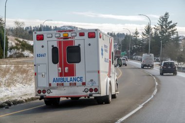 Victoria, British Columbia, Canada. Feb 10, 2025. BC Ambulance vehicle rear view, driving on a snowy roadside with emergency lights flashing, emphasizing the vital role of emergency services. clipart