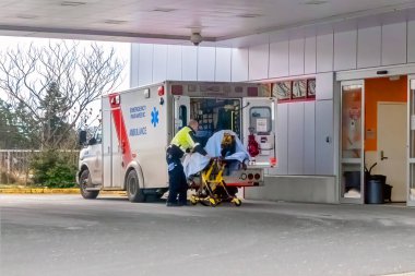 Victoria, British Columbia, Kanada. 14 Şubat 2025. BC Acil Sağlık Servisi 'nden bir sağlık görevlisi, Kanada, Victoria' da bir hastanenin acil çıkışında sedyeye bağlı bir hastaya yardım ediyor..