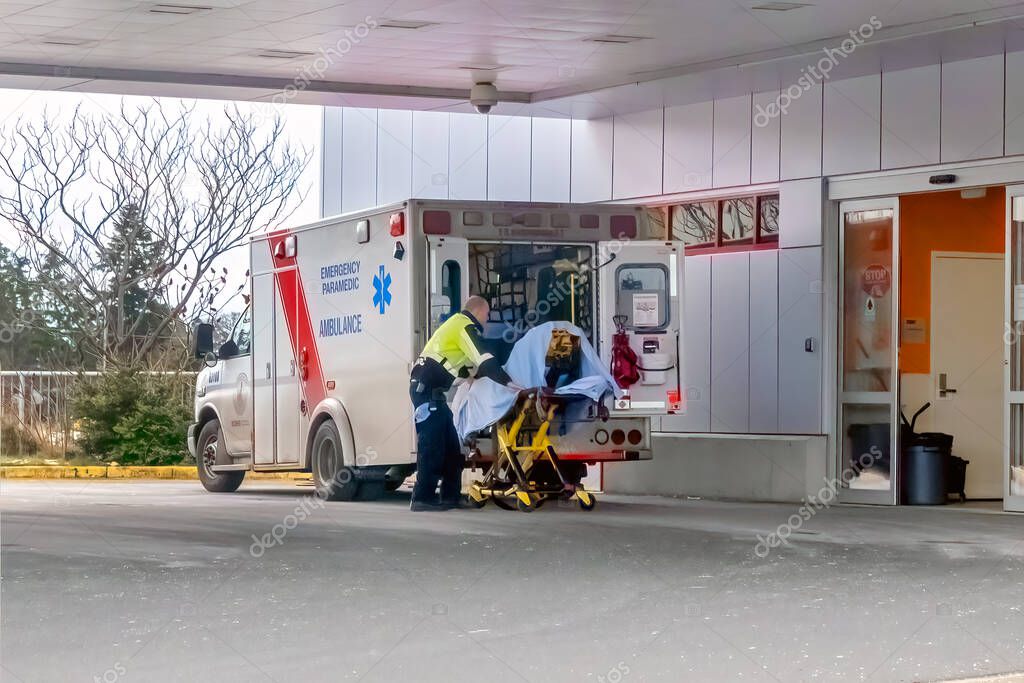 Victoria, British Columbia, Canada. Feb 14, 2025. A BC Emergency Health Services paramedic assists a patient on a stretcher outside a hospital emergency entrance in Victoria, Canada.
