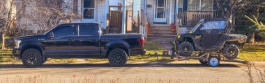 Calgary, Alberta, Kanada. Mar 2, 2025. Siyah bir Ford F-150 kamyonu yerleşim yerindeki bir caddeye park etmiş, bir karavanda Polaris RZR çekiyor..