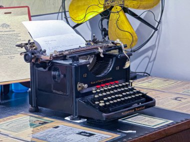 Victoria, BC, Kanada. Mar 1, 2025. Klasik Remington Standard 12 daktilo, tarihsel ofis teknolojisine göz atma imkanı sunan belgeler ve bir vantilatör ile sergileniyor..