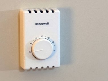 Calgary, Alberta, Kanada. Mar 1, 2025. Açık renkli bir duvara 15 dereceye ayarlı beyaz bir Honeywell termostatı monte edilir. Cihaz basit ve işlevsel..