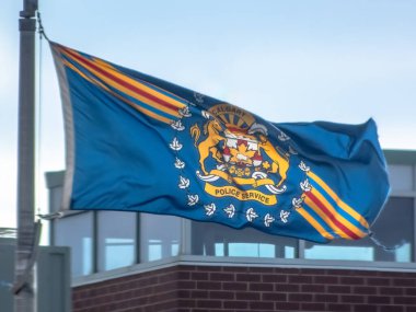 Calgary, Alberta, Kanada. 12. kat, 2025. Calgary Polis bayrağı mavi gökyüzüne karşı direkte dalgalanıyor, bina aşağıda görünüyor. Parlak bir gün, atlarla ve akçaağaç yaprağıyla amblem..