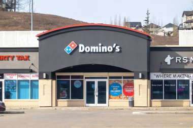 Calgary, Alberta, Kanada. 23 Aralık 2025. Bir alışveriş merkezindeki Domino 's Pizza mağazasının sokak seviyesinde çekilmiş bir fotoğrafı. Logosu ve vitrininde promosyon tabelaları var..