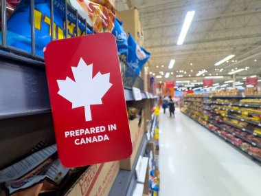 Calgary, Alberta, Kanada. 23 Aralık 2025. Beyaz bir akçaağaç yaprağıyla kırmızı bir tabelanın yakın çekimi ve arka planda bulanık koridorlar bulunan bir market rafına yerleştirilmiş 
