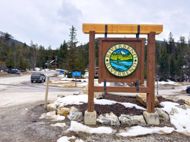 Panorama, British Columbia, Kanada. 31 Aralık 2025. Nehirbükücü için tahta tabela dairesel logoyla kavşakta, karla kaplı zeminde ve bulutlu bir gökyüzünün altında uzak dağlarda duruyor..