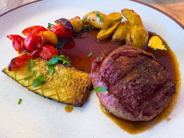 Güzel kaplanmış bir tabakta kızartılmış patates, domates ve kabak soslu kurutulmuş sığır eti madalyonu benekli seramik bir tabakta zengin bir sos serpiştiriliyor..