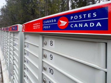 Panorama, British Columbia, Kanada. 31 Aralık 2025. Bir sıra Kanada Posta Posta Kutusu, numara 1-12, uzaklığa uzanıyor, simgesel kırmızı ve mavi logo belirgin bir şekilde sergileniyor.
