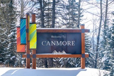 Canmore, Alberta, Kanada. 2 Nisan 2025. Renkli pankartlı Canmore tabelasına hoş geldiniz. Her zaman yeşil ağaçlarla kaplı, karlı bir arazide duruyor..