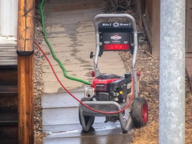 Calgary, Alberta, Kanada. 2 Nisan 2025. Briggs ve Stratton basınçlı çamaşır makinesi ıslak beton bir yolda duruyor, yanında da yeşil bir hortum var..