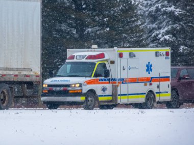 Banff, Alberta, Kanada. 2 Nisan 2025. Karlı bir yolda bir ambulans sürüyor, solunda bir kamyon ve sağında bir araba, karlı bir ormanın ortasında..
