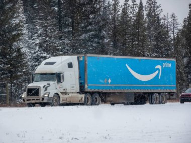 Banff, Alberta, Kanada. 31 Aralık 2025. Açık mavi Amazon Prime karlı bir yolda ormanın içinden geçen beyaz bir kamyonet..