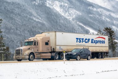 Calgary, Alberta, Kanada. 5 Nisan 2025. Bir TST-CF yarı kamyonet, karlı bir otoyolda koyu renkli bir cipin yanında seyahat ediyor. Arkada karla kaplı dağlar ve ağaçlar var..