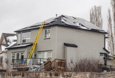 Calgary, Alberta, Kanada. 4 Nisan 2025. Calgary 'de iki katlı bir evin çatısına güneş panelleri kurulmuş ve yan tarafında sarı bir merdiven var. Çatıda ve yerde biraz kar kaldı..
