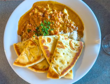 Beyaz bir tabakta kişniş ile süslenmiş bir tabak tereyağlı tavuk ya da tavuk tika masala naan ekmeği ve pilav sunulur..