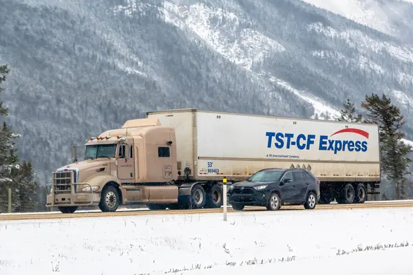 Calgary, Alberta, Kanada. 5 Nisan 2025. Bir TST-CF yarı kamyonet, karlı bir otoyolda koyu renkli bir cipin yanında seyahat ediyor. Arkada karla kaplı dağlar ve ağaçlar var..