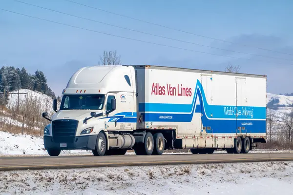 Calgary, Alberta, Kanada. 4 Nisan 2025. Beyaz bir Atlas Van Lines yarı kamyonet, mavi ve kırmızı aksanlı, AMJ Calgary tarafından işletiliyor, Calgary, Alberta 'da karlı bir yolda ilerliyor..