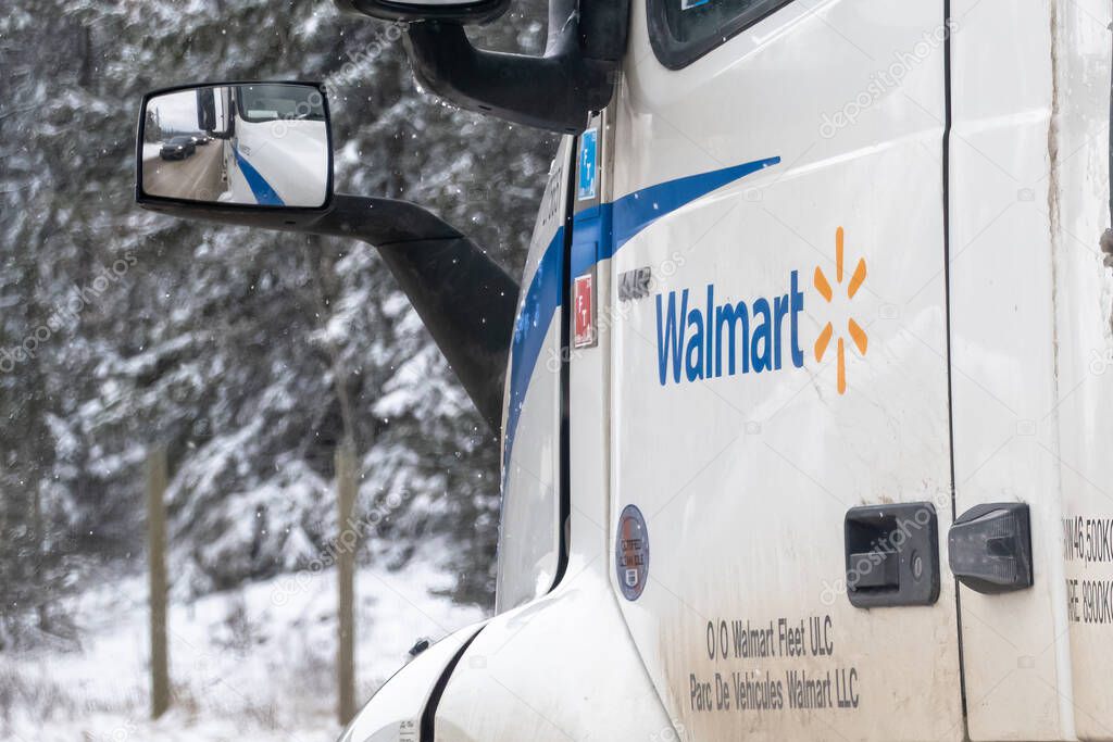 Banff, Alberta, Canada. Apr 5, 2025. A white Walmart semi-truck shows its logo and fleet details. Snow-covered trees are visible in the side mirror, suggesting a winter setting.