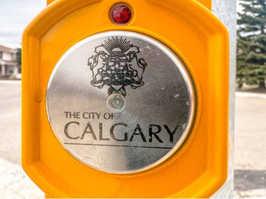 Calgary, Alberta, Kanada. 10 Nisan 2025. Yakın plan, Calgary şehrinin simsiyah logosunun sarı bir kovan içinde gümüş bir plaka üzerinde yer aldığı yaya geçidinde bir itme düğmesi gösteriyor..