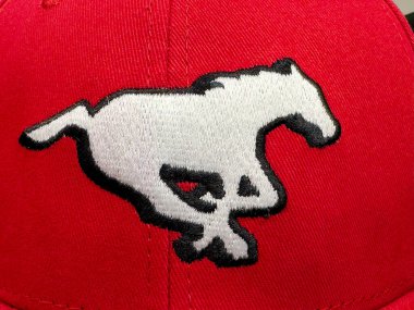 Calgary, Alberta, Kanada. 10 Nisan 2025. Yakın planda beyaz Calgary Stampeders at logosu görünüyor, siyah çizilmiş, kırmızı bir şapka üzerine işlenmiş..