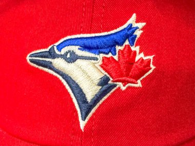 Calgary, Alberta, Kanada. 10 Nisan 2025. Yakın çekimde Toronto Blue Jays logosu kırmızı bir beyzbol şapkasına işlenmiş. Logoda kırmızı akçaağaç yaprağıyla mavi bir karga kafası var..