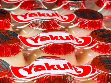 Calgary, Alberta, Kanada. 10 Nisan 2025. Marka logosunu gösteren kırmızı ve beyaz folyo kapaklı birçok Yakult şişesinin yakın çekimi.