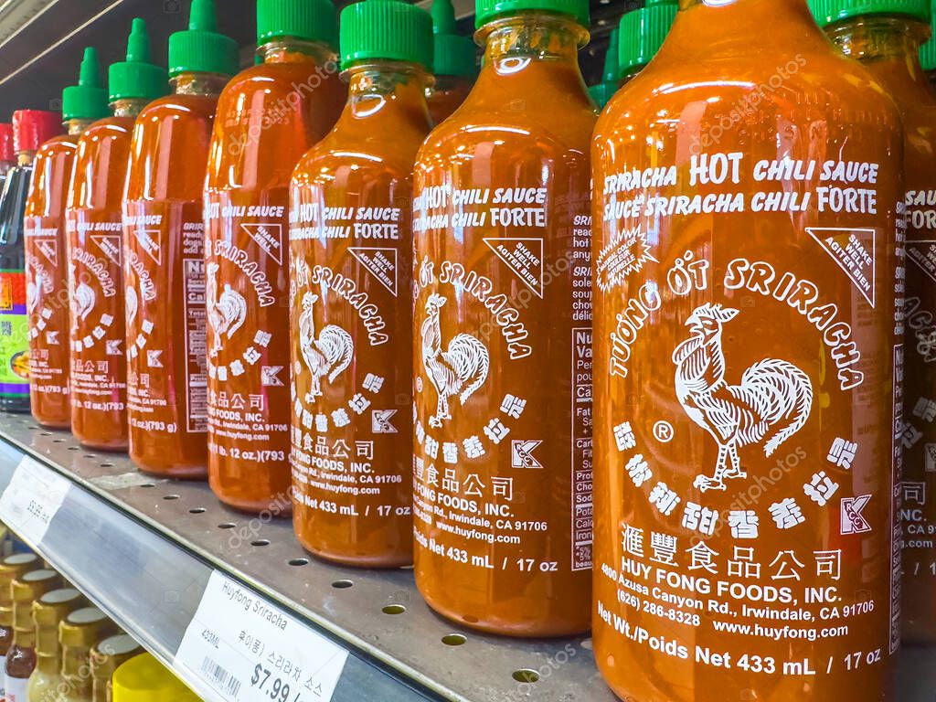 Calgary, Alberta, Canada. Apr 10, 2025. A shelf displays multiple bottles of Huy Fong Sriracha hot chili sauce, recognized by their white rooster logo and green caps.
