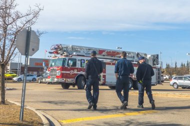 Calgary, Alberta, Kanada. 13 Nisan 2025. Üniformalı üç itfaiyeci, bulutlu bir gökyüzünün altındaki otoparkta geniş bir merdivenle Calgary İtfaiyesi 'nin kamyonuna doğru yürüyorlar..
