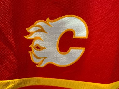 Calgary, Alberta, Kanada. 17 Nisan 2025. Calgary Flames hokey takımının logosu kırmızı forma ya da kumaş üzerinde belirgin bir şekilde sergileniyor..