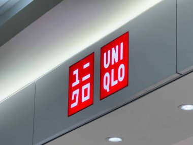 Calgary, Alberta, Kanada. 16 Nisan 2025. Parlak ışıklı bir UNIQLO mağaza tabelası tarafsız gri bir duvara karşı sergileniyor. Kırmızı dikdörtgen logolarda markanın adı İngilizce ve Japonca olarak geçiyor..