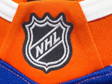 Edmonton, Alberta, Kanada. 16 Nisan 2025. Mavi ve beyaz aksanlı turuncu bir kumaş üzerinde NHL logosu, üzerinde 