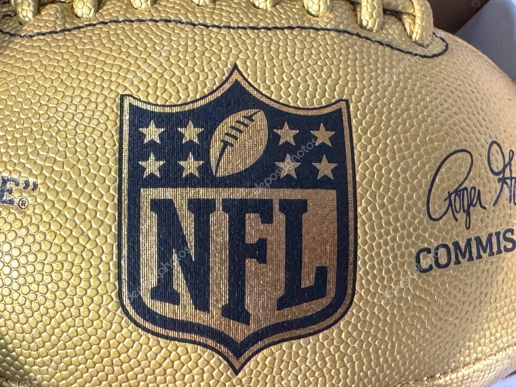 Calgary, Alberta, Canada. Apr 17, 2025. A close-up shot of the NFL logo on a gold-colored textured football, showing stitching and surface detail.