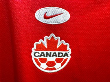 Calgary, Alberta, Kanada. 17 Nisan 2025. Kanada futbol logosu (akçaağaç yaprağı ve futbol topu) ve kırmızı spor kumaşında bir Nike amblemi..