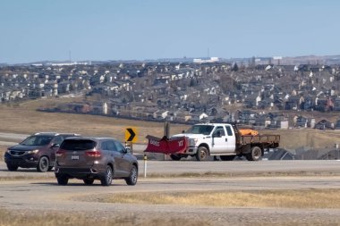 Calgary, Alberta, Kanada. 18 Nisan 2025. Üç araçlı güneşli bir gün: kahverengi bir SUV, koyu renk bir SUV, ve kar küremeli beyaz bir kamyon, yayılan bir banliyö manzarasının arka planına karşı.